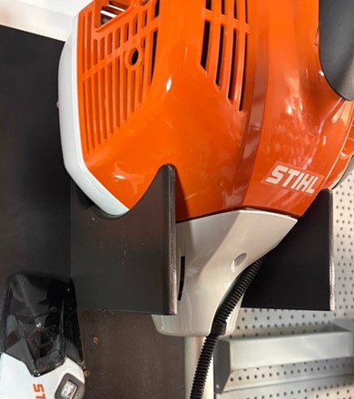 Wzmocniony pomarańczowy uchwyt ścienny z druku 3D do profesjonalnej kosy spalinowej STIHL FS 460 zamontowany na ścianie.