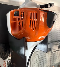 Wzmocniony pomarańczowy uchwyt ścienny z druku 3D do profesjonalnej kosy spalinowej STIHL FS 460 zamontowany na ścianie.