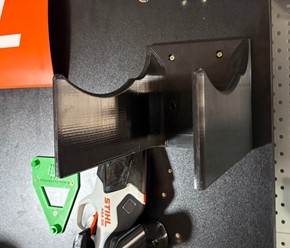 Wzmocniony pomarańczowy uchwyt ścienny z druku 3D do profesjonalnej kosy spalinowej STIHL FS 460 zamontowany na ścianie.